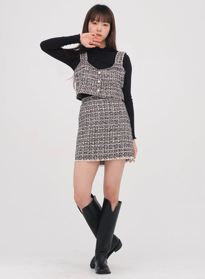 Tweed Bustier #1210o182 in black-white tweed, three-quarter front view on model with raised hand pose, V-neckline and frayed strap detail visible, paired with black long-sleeve top and tweed mini skirt.