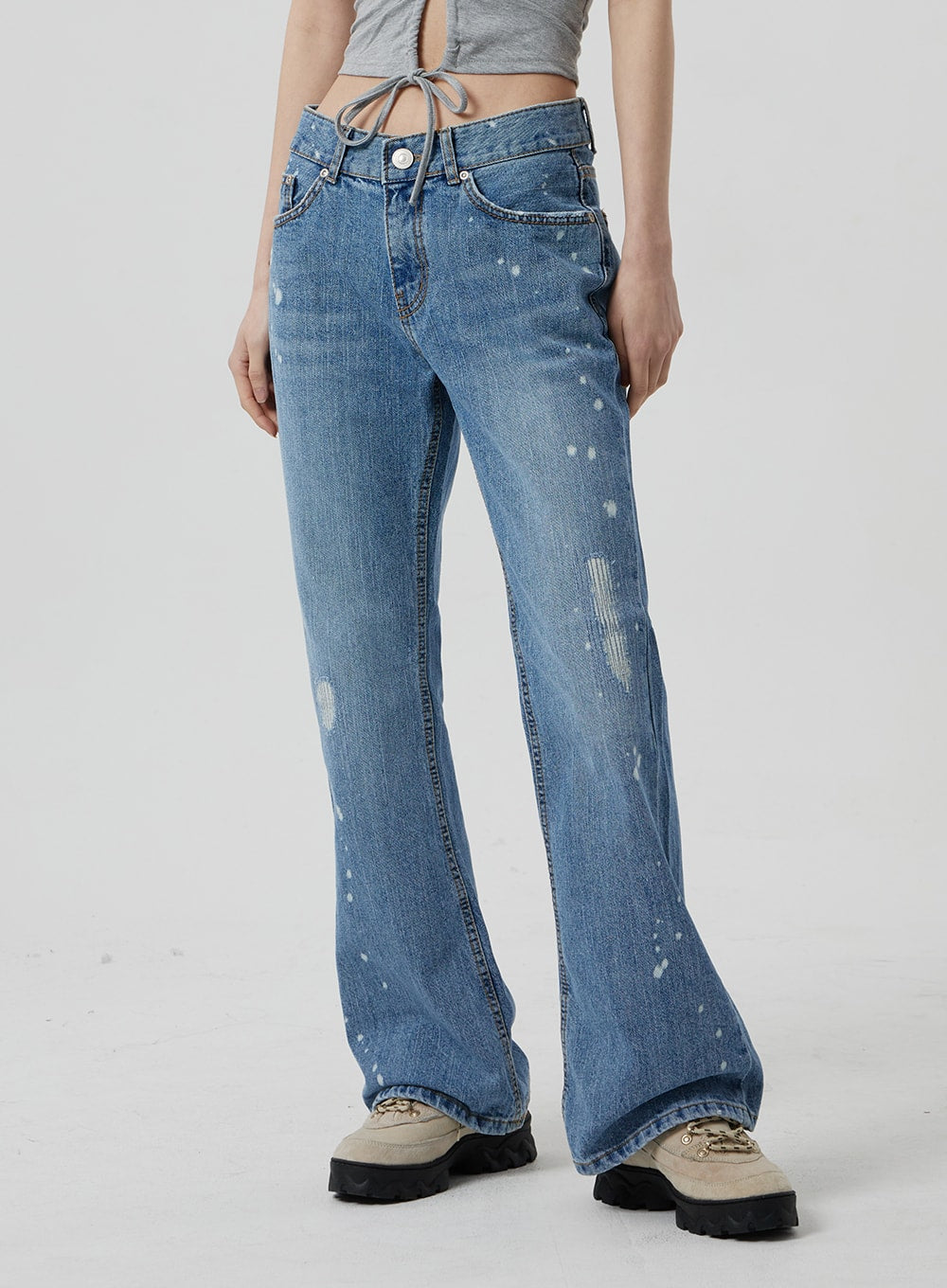Low Rise Bootcut Jeans CF309 in blue denim, front close-up on model from waist to ankle, low waist button fly, paint-splatter detailing and abrasion distressing on slim bootcut leg.