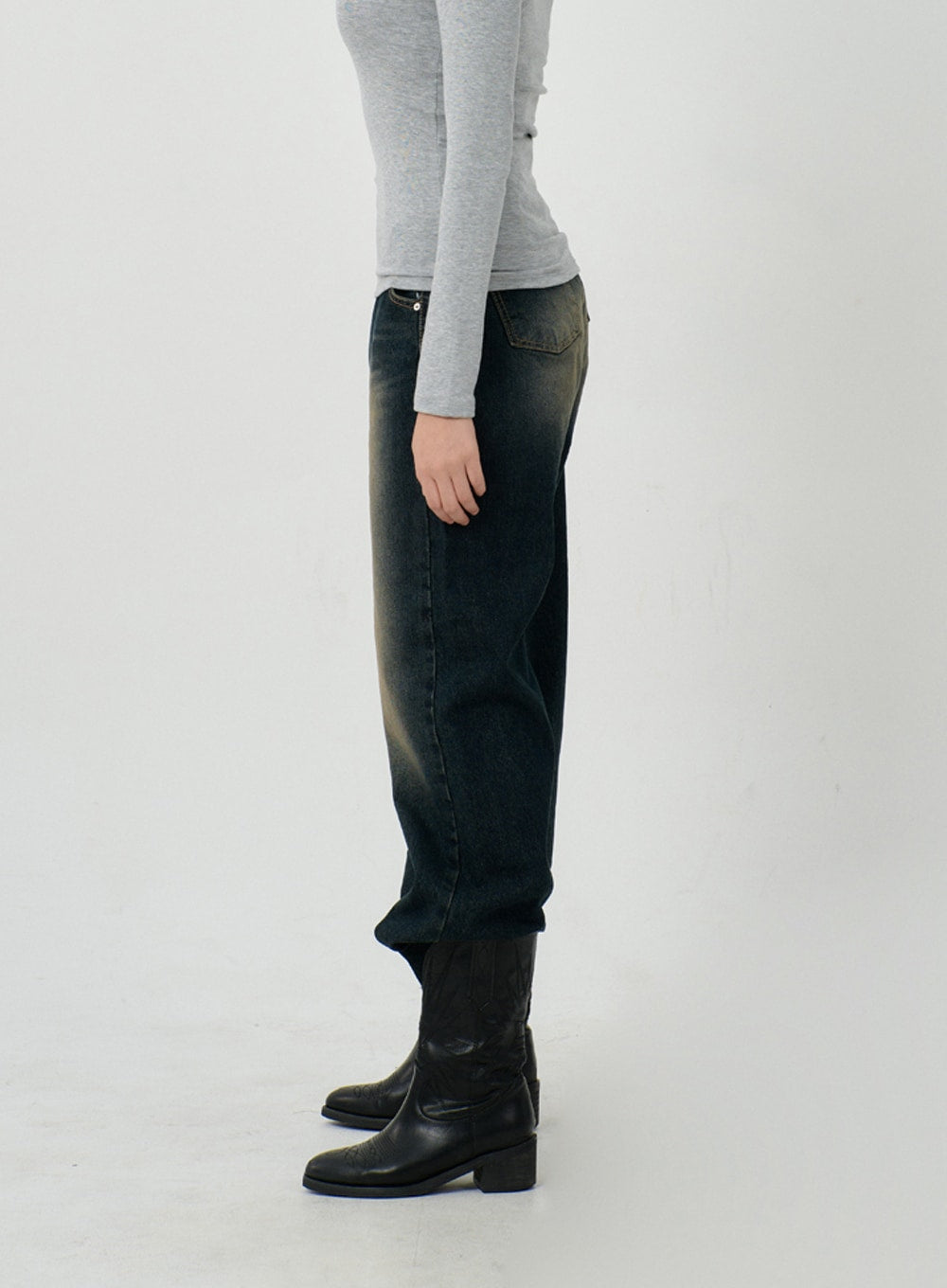 Vintage Washing Baggy Jeans ID23 in dark indigo, side view on model, wide-leg silhouette with vintage yellow fade wash, back pocket visible, styled with grey long-sleeve top and black boots.