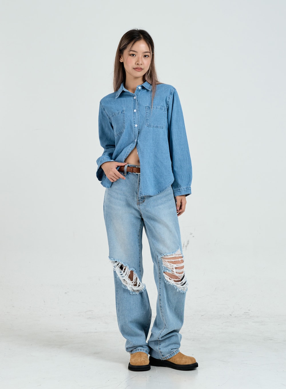 Ripped Maxi Denim Pants Unisex CO14 in light blue, full-body front view on model, wide-fit destroyed denim with frayed knee tears, styled with denim shirt and brown belt.