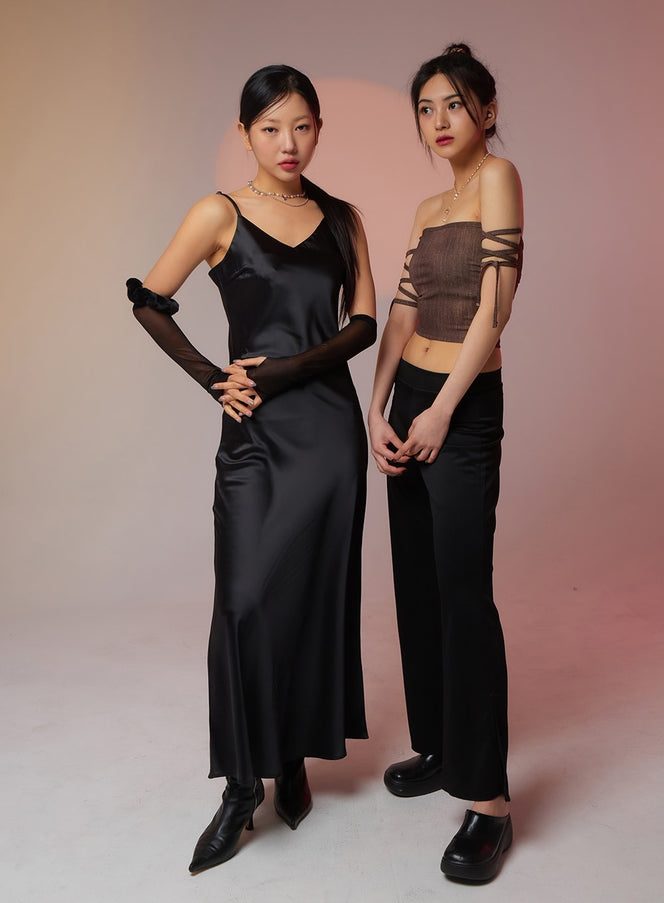 Satin Maxi Dress BF323 in black, full-length front pose on left model, sleeveless V-neck satin slip maxi with fluid bias-cut hem, paired with black mesh gloves and ankle boots.