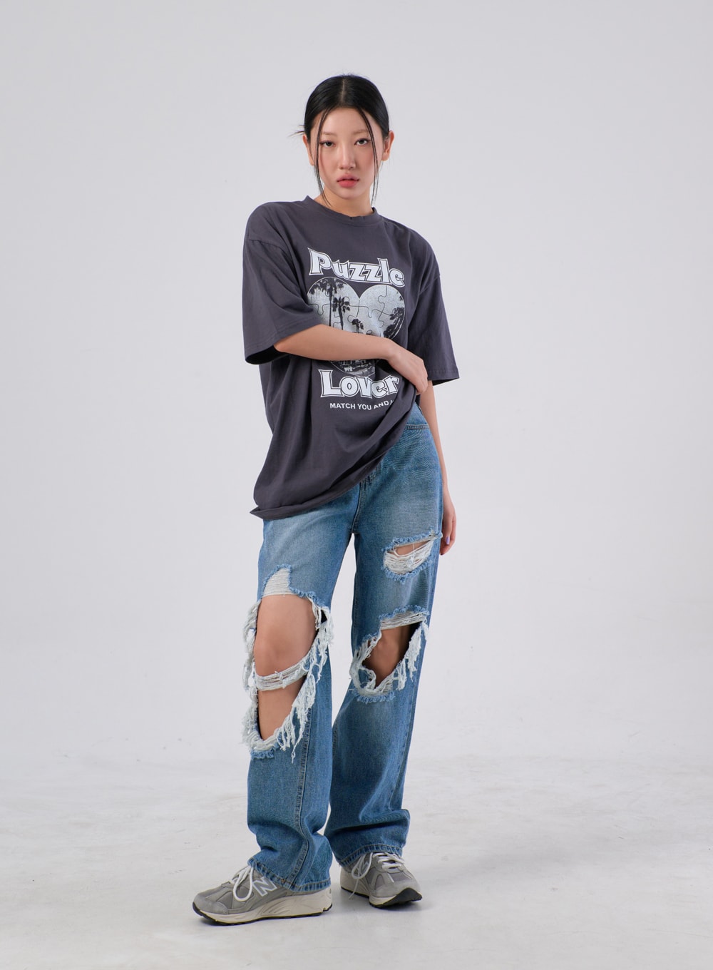 Ripped Knee Jeans IA305 in medium blue, full-body front shot on model with relaxed pose, wide cotton denim with heavy destroyed knee openings, paired with oversized grey graphic tee.