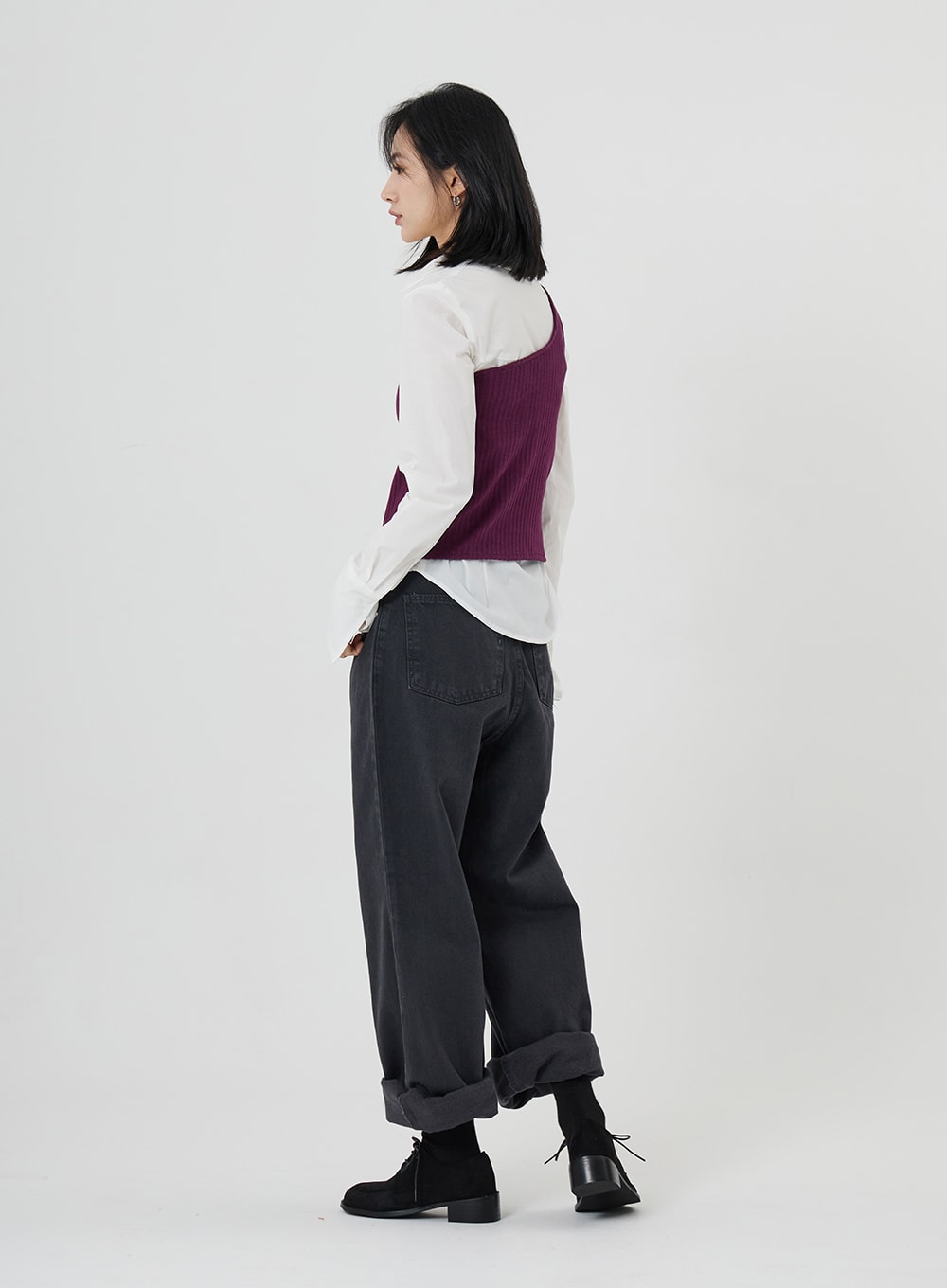 Maxi Denim Pants ON23 in charcoal grey, back view on model, wide-leg cotton denim with rolled cuffs and visible back pockets, styled with white shirt and purple ribbed vest.