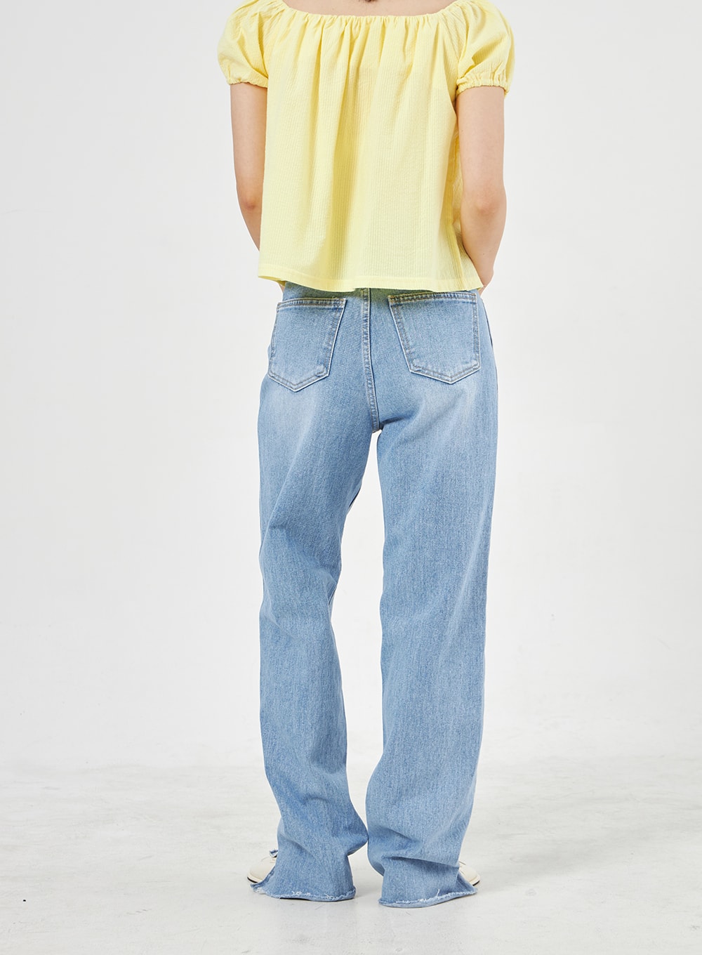 Light Wash Jeans OA310 in light blue, back view on model, wide-fit washed denim with dual back pockets and side slit at hem, worn with yellow puff-sleeve crop top.