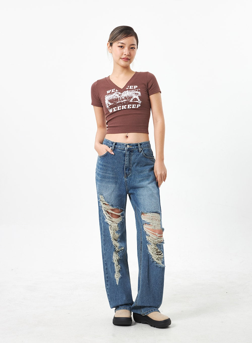 Wide Ripped Jeans CA304 in medium blue, full-body front on model with relaxed stance, wide-fit washed denim featuring multi-rip knee distressing, paired with brown graphic crop tee.