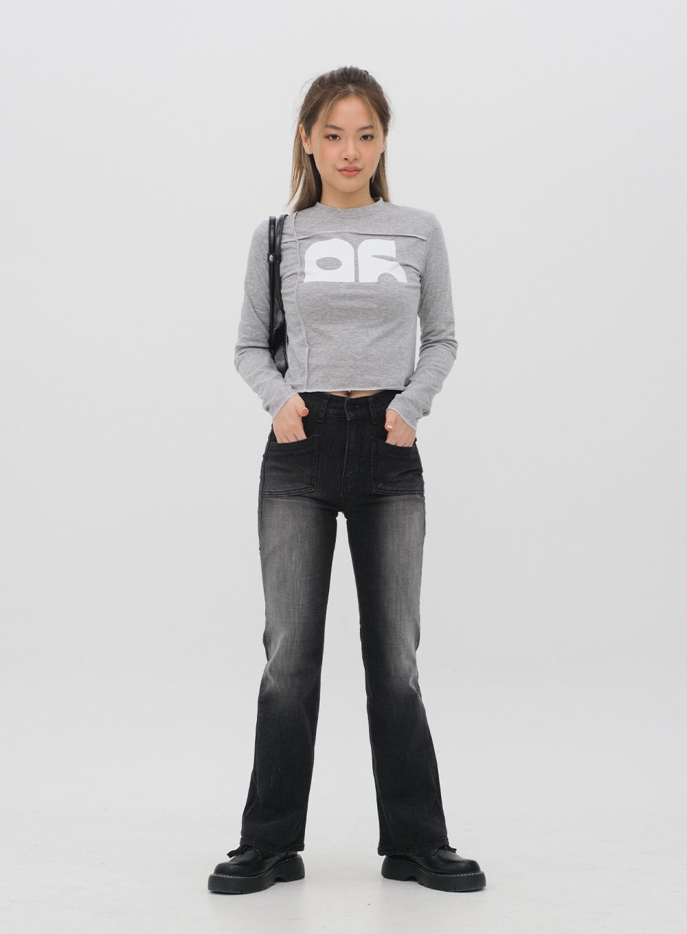 Bootcut Jeans M4 in black gradation wash, front full-body shot on model with hands in pockets, long bootcut leg, paired with grey graphic crop top and black shoulder bag.