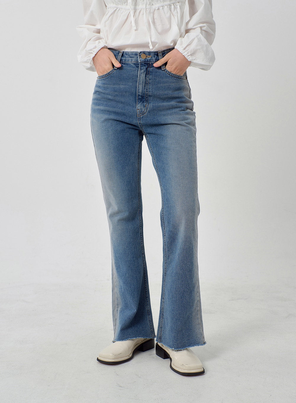 Light Washed Bootcut Jeans OD27 in light blue, front mid-body close-up on model, high-rise waistband with hands in pockets, slim-fit washed cotton denim, raw frayed bootcut hem visible.