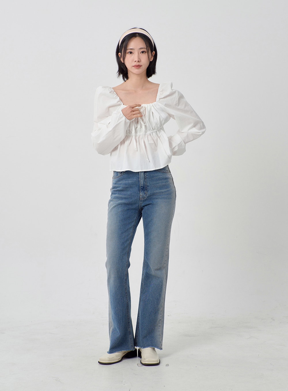 Light Washed Bootcut Jeans OD27 in light blue, front full-length shot on model, high-rise slim-fit washed cotton denim, bootcut silhouette with raw hem, styled with white puff-sleeve blouse.