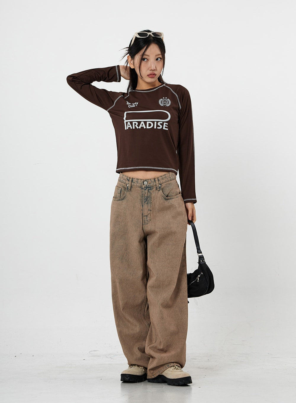 Raemon Wide Jeans Unisex CS21 in brown acid-wash, full front view on model with hand raised, ultra-wide leg silhouette with brown tonal styling and chunky sneakers.