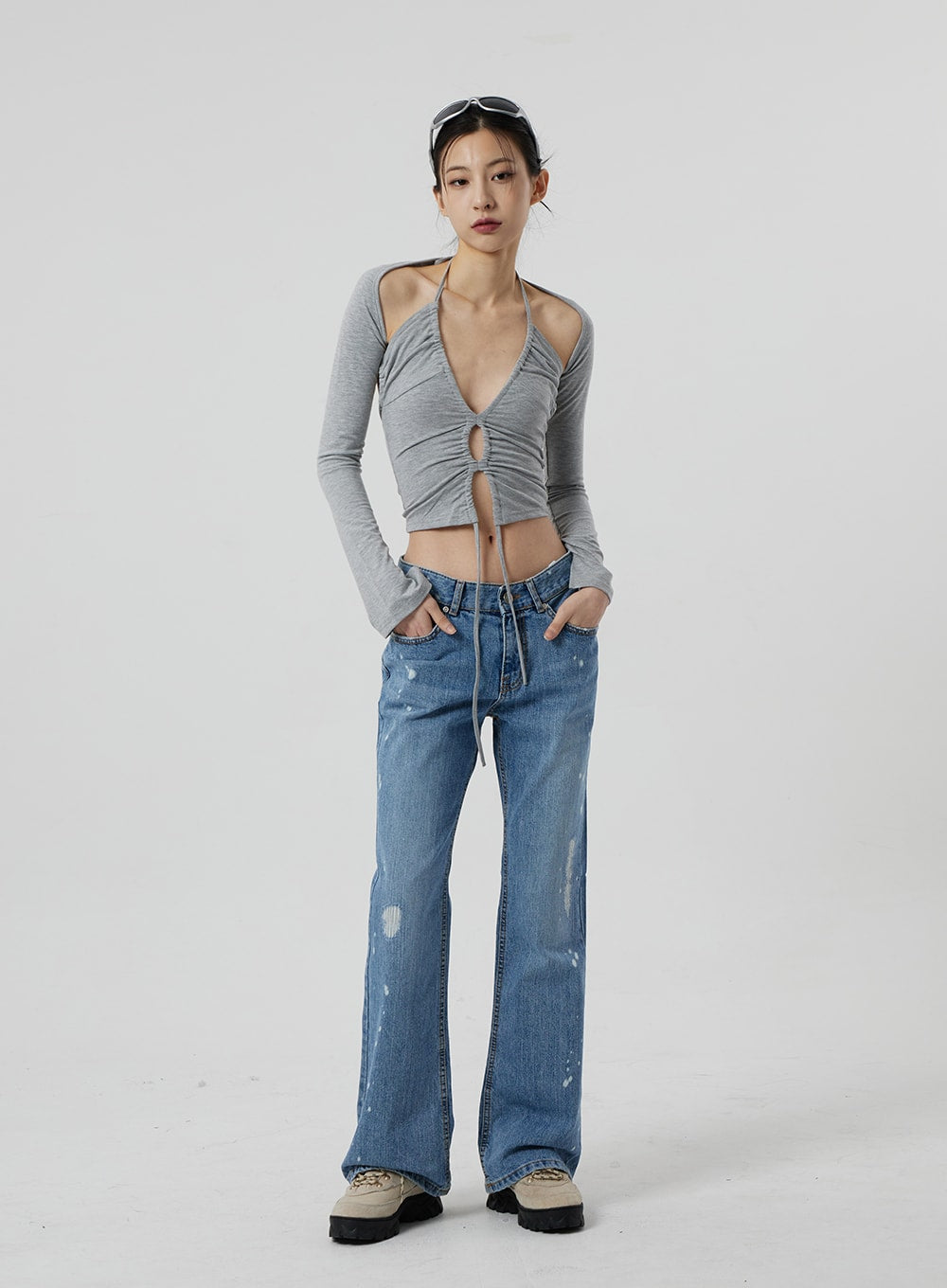 Low Rise Bootcut Jeans CF309 in blue denim, full-length front view on model, hands in pockets, slim bootcut silhouette with paint-splatter and distressing, paired with grey ruched crop halter top.
