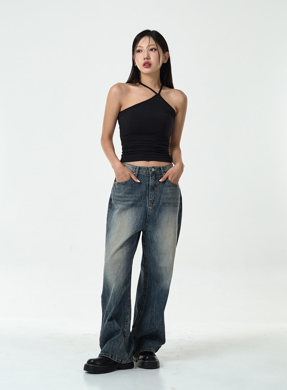 Washed Denim Pants CG10 in dark blue, three-quarter front view on model, relaxed wide-leg denim with washed gradient, hands in pockets, styled with black asymmetric halter top.
