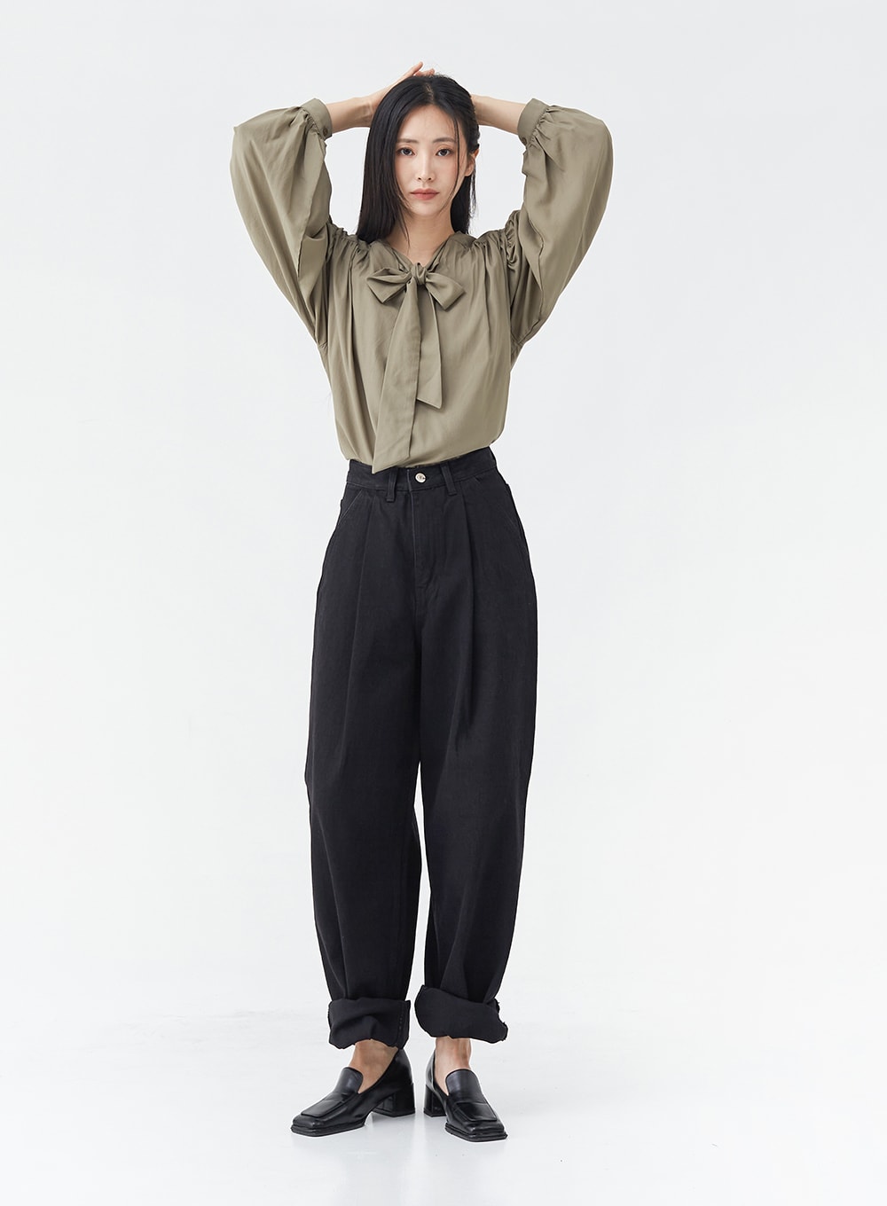 Pintuck Black Jeans OG18 in black, full-body front shot on model with arms raised, wide-fit cotton pintuck jeans with rolled cuffs, styled with olive bow blouse and black loafers.