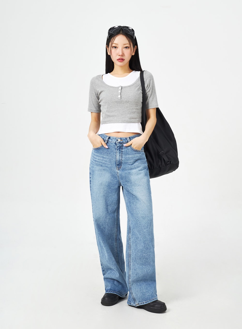 Mid-Wash Bootcut Jeans CM323 in mid blue, full-length front view on model with hands in pockets, wide-fit washed denim styled with grey crop top and large black tote bag.