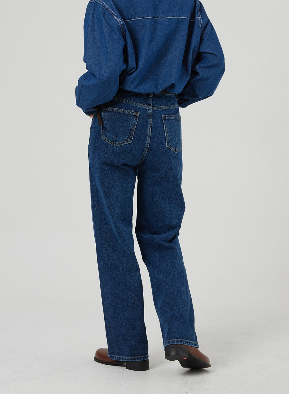 Basic Indigo Jeans OF310 in indigo, back view waist-to-hem close-up on model, showing dual back pockets, clean seam lines, and wide-leg hem, worn with denim shirt and brown boots.