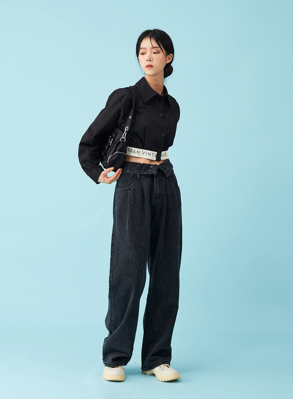 Four Buttoned Open Black Jeans CU8 in washed black, front three-quarter view on model looking down, relaxed wide-leg silhouette, logo belt visible at low waist, paired with black crop shirt and crossbody bag.