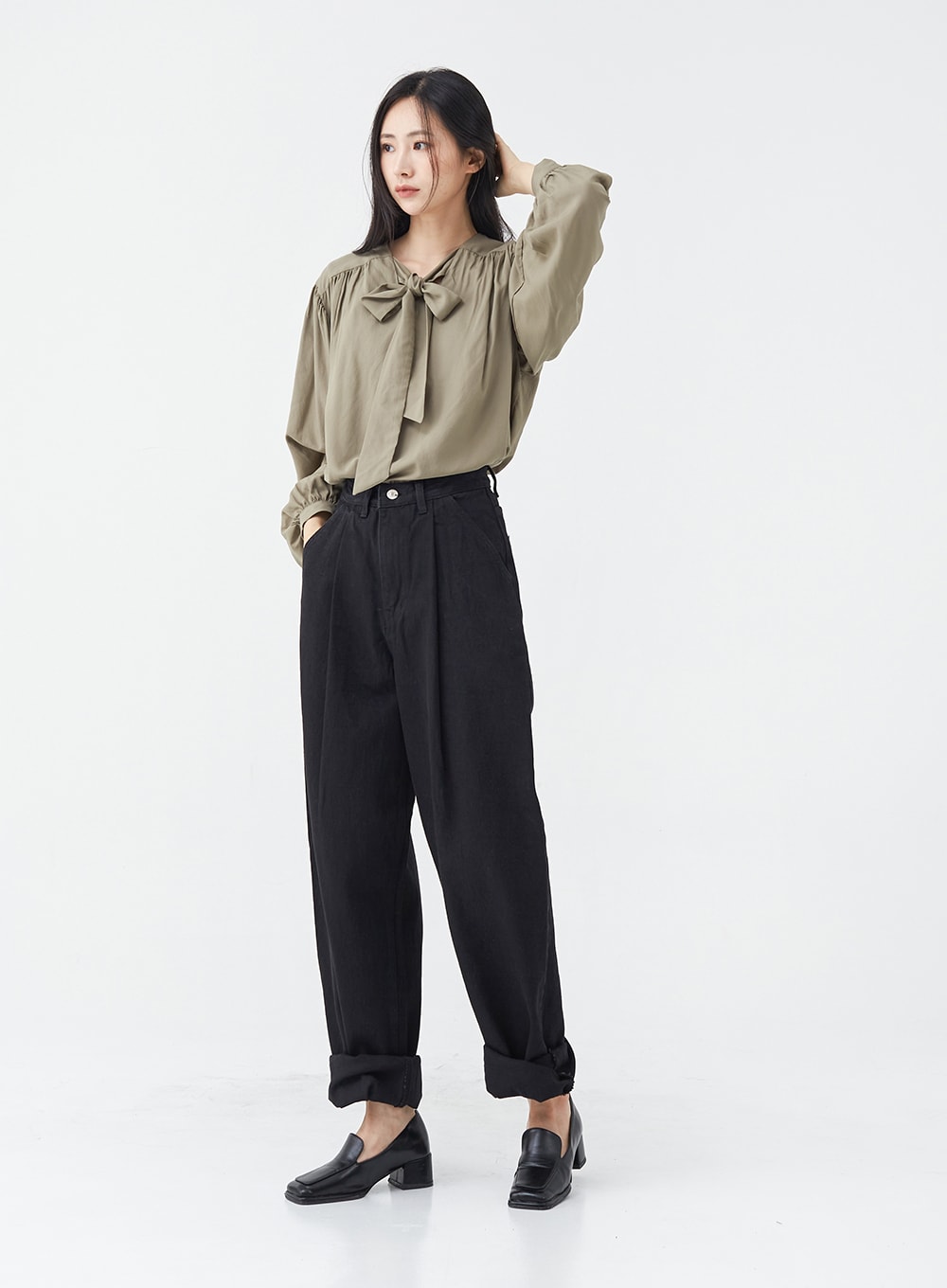 Pintuck Black Jeans OG18 in black, three-quarter front angle on model, wide-fit cotton pintuck jeans with rolled cuffs, hand in hair pose, styled with olive bow blouse and loafers.