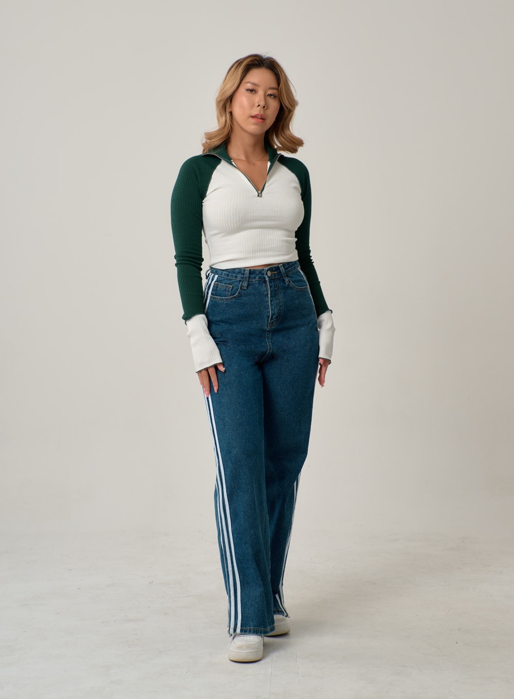 Side Stripes Straight Leg Jeans IN22 in mid blue, full-body front shot on model walking, wide-fit high-rise denim with bold white side stripes, styled with colorblock zip crop top and white sneakers.