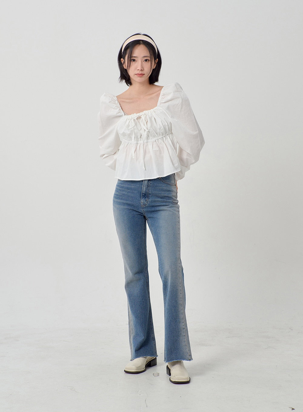 Light Washed Bootcut Jeans OD27 in light blue, front full-body shot on model with relaxed pose, slim-fit washed denim, bootcut leg with raw hem, paired with white puff-sleeve top and white loafers.