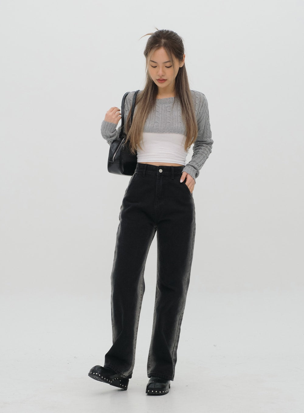 Black Jeans C1002 in washed black, full-body front shot, model looking down with hand in pocket, wide-leg silhouette, high waist, styled with grey cable-knit crop and black bag.