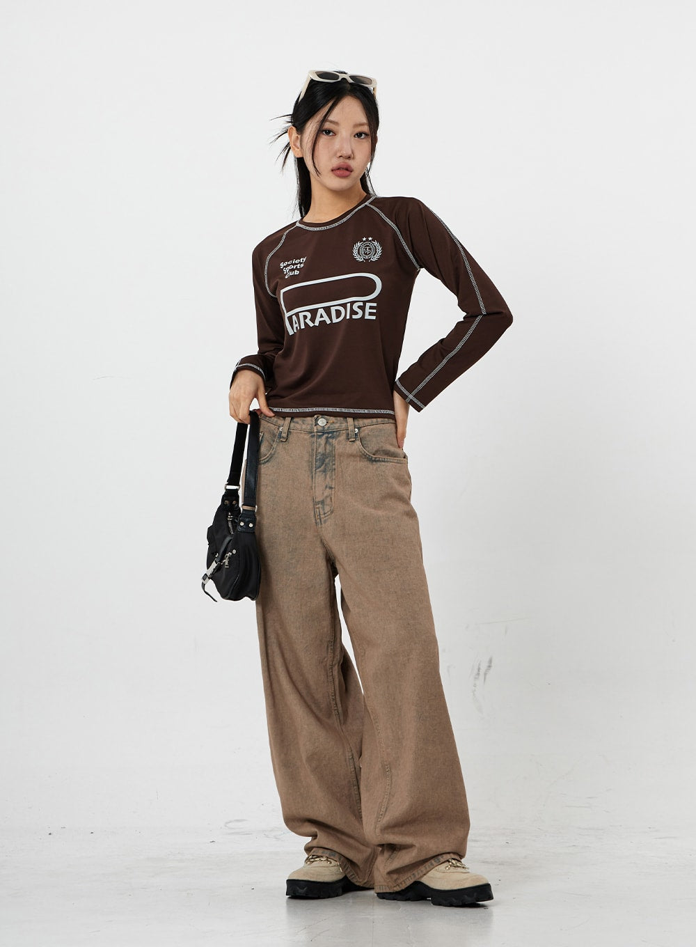 Raemon Wide Jeans Unisex CS21 in brown acid-wash, three-quarter front angle on model standing with hand on hip, relaxed wide-leg fit with slouchy drape, casual tomboy look.