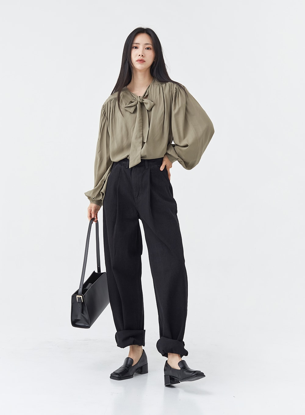 Pintuck Black Jeans OG18 in black, full-body slight angle on model holding black tote, wide-fit cotton pintuck jeans with rolled cuffs, paired with olive bow blouse and loafers.