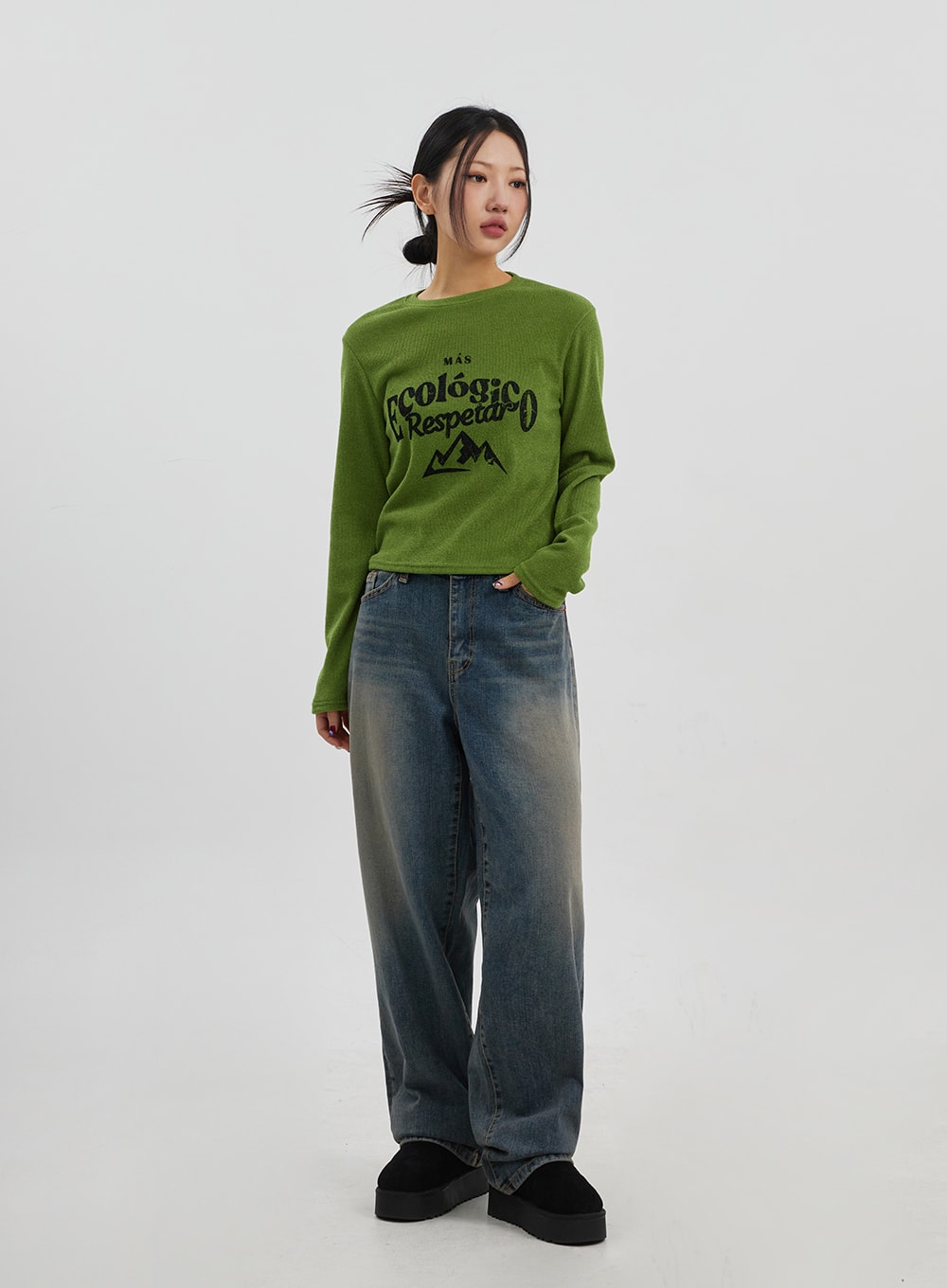 Mid-Rise Baggy Jeans Unisex CJ330 in vintage blue, full-body slight side view on model, wide-leg cotton denim with vintage fading, styled with green graphic knit top.