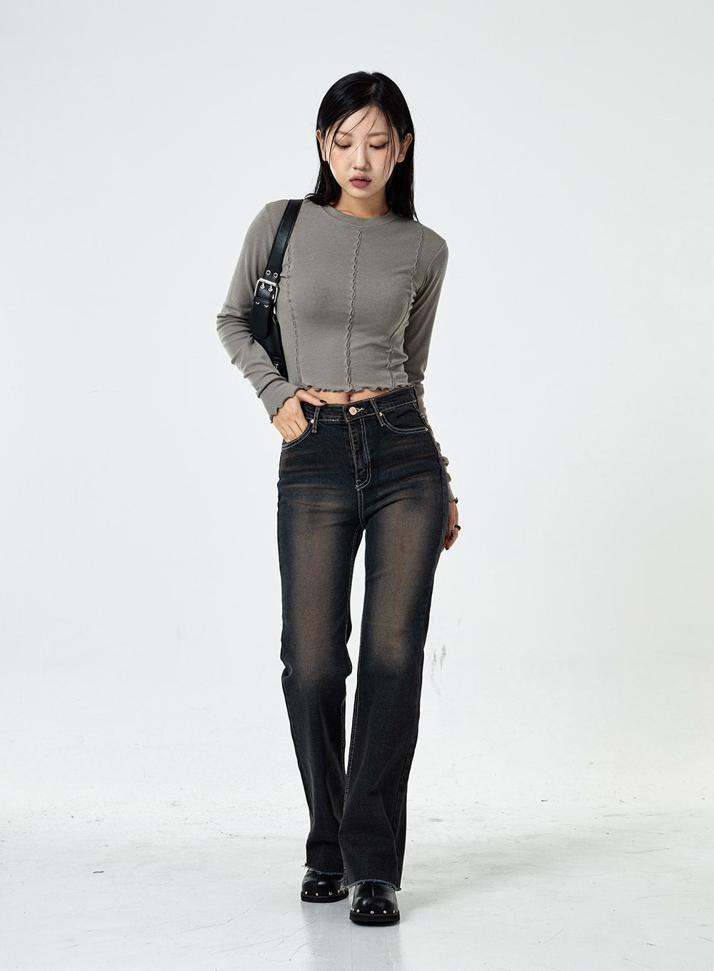 Basic Washed Bootcut Jeans CS07 in black washed denim, full-length front view on model looking down, high-waist slim bootcut, faded wash, paired with grey long-sleeve crop top and shoulder bag.