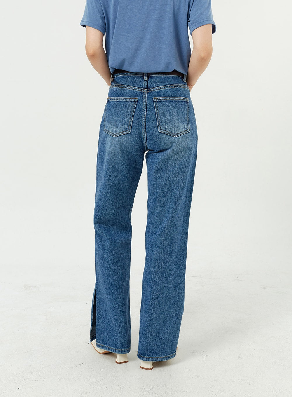 Side Slit Jeans OM308 in mid blue, back view waist-to-hem on model, wide-leg cotton denim showing dual back pockets and subtle side slit at hem, white boots.