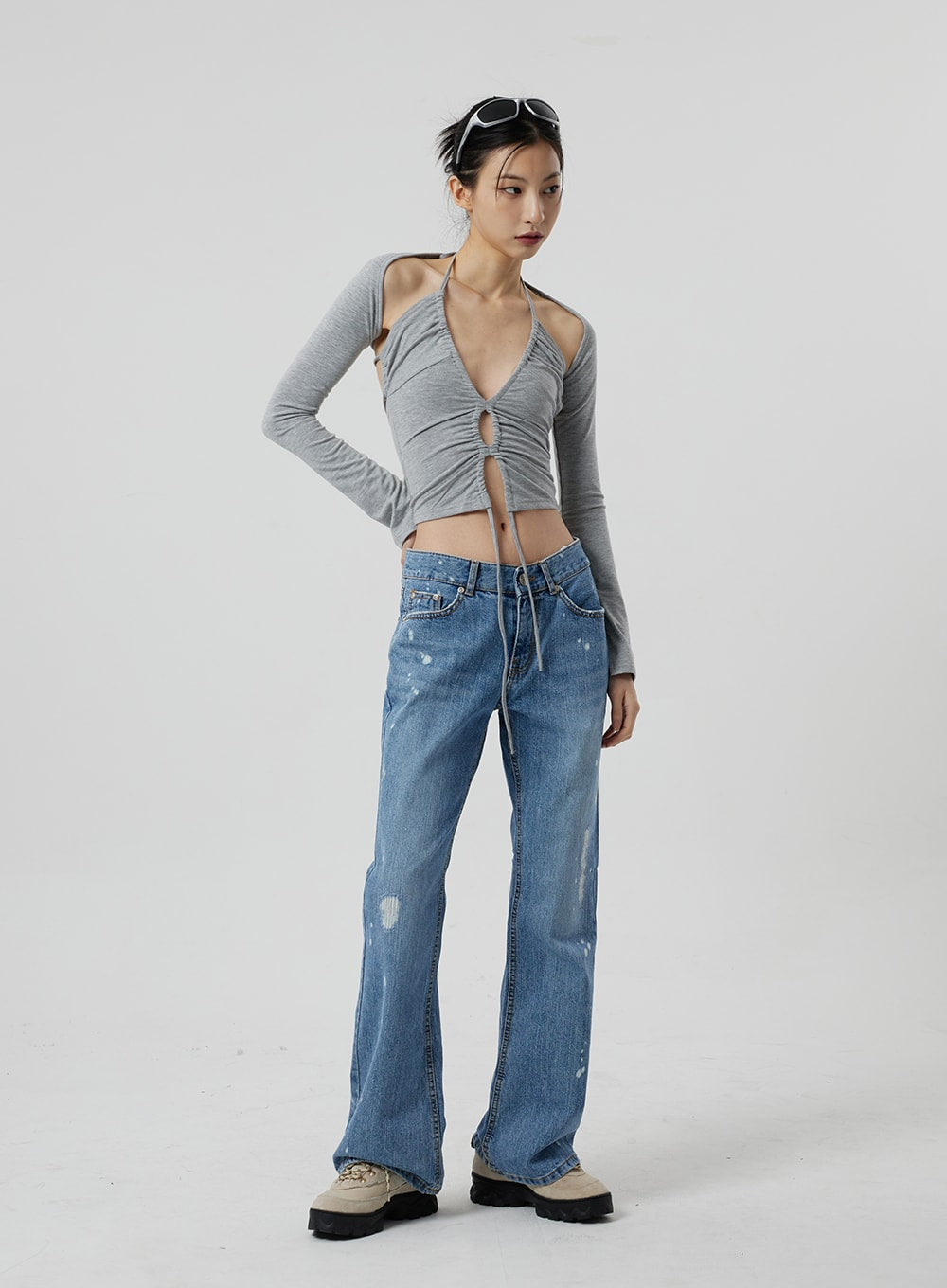 Low Rise Bootcut Jeans CF309 in blue denim, front three-quarter view on model, one hand on hip, low waist with worn-in fading and paint-splatter detail, bootcut leg, styled with grey halter crop top.
