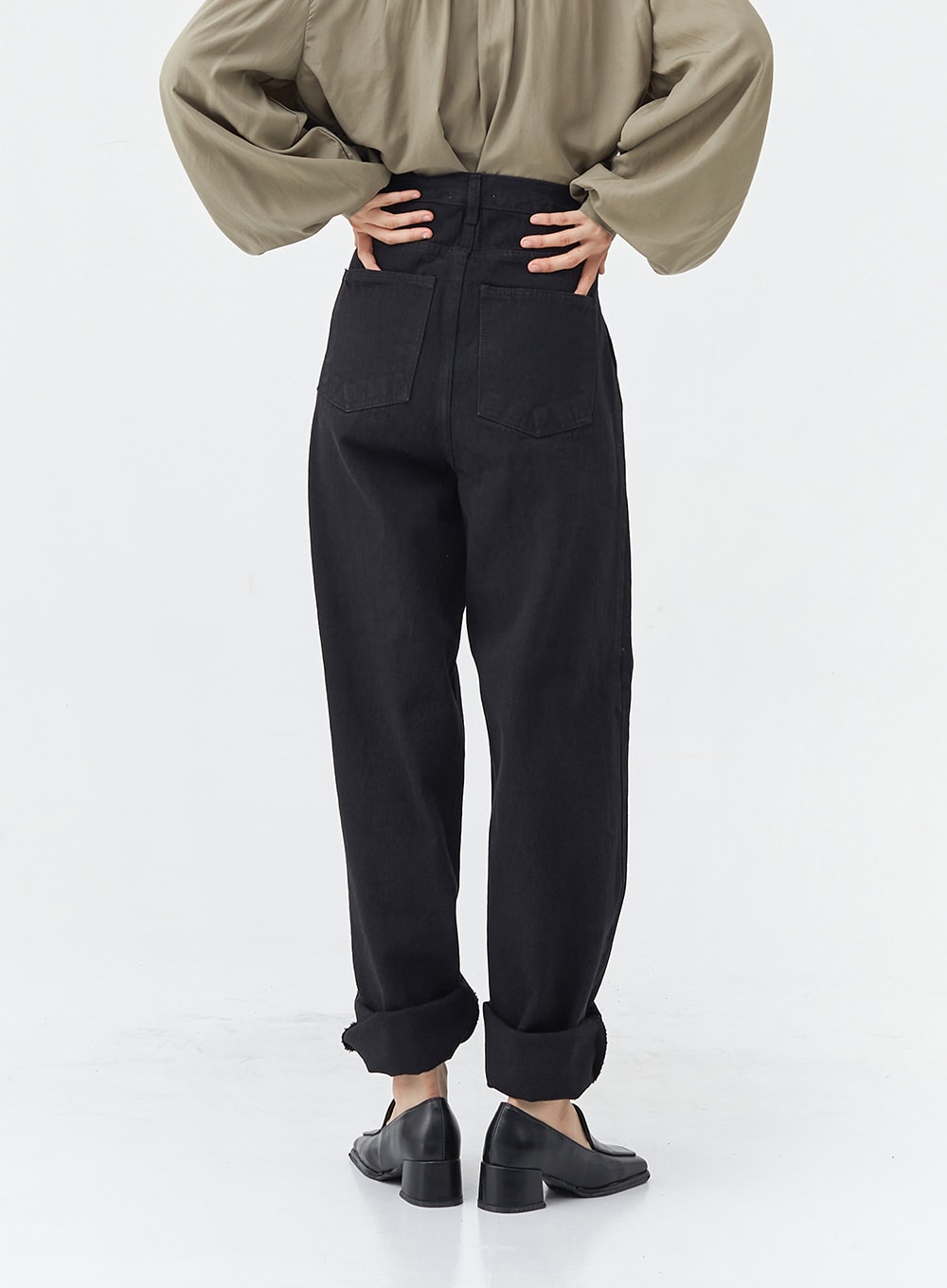 Pintuck Black Jeans OG18 in black, back view on model, wide-fit cotton with patch back pockets and rolled cuffs, high-rise waistband, paired with olive blouse and black loafers.