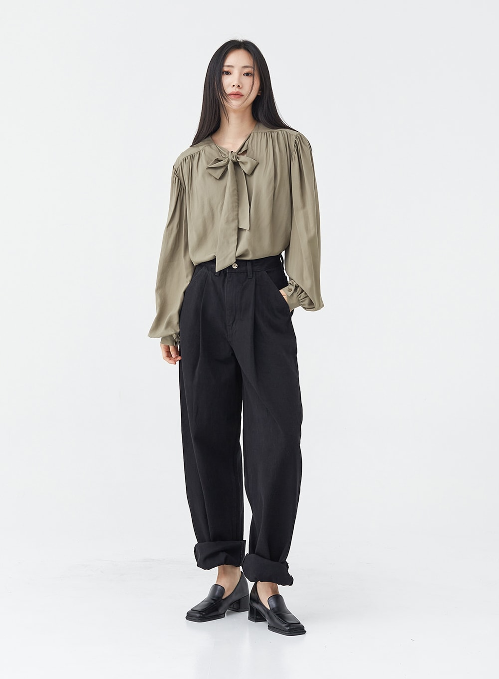 Pintuck Black Jeans OG18 in black, full-body slight side-front view on model, wide-fit cotton pintuck jeans with rolled hem, styled with olive bow blouse and black loafers, neutral pose.