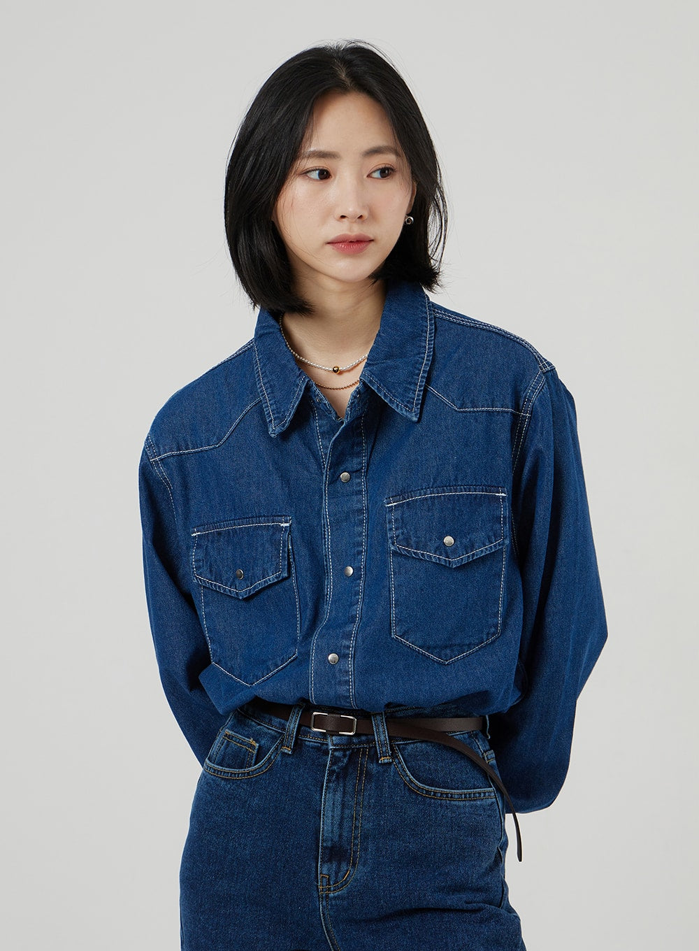 Basic Indigo Jeans OF310 in indigo, upper-body front shot on model, high-rise waistband and front pockets visible, belted, paired with blue denim western shirt and pearl necklace.