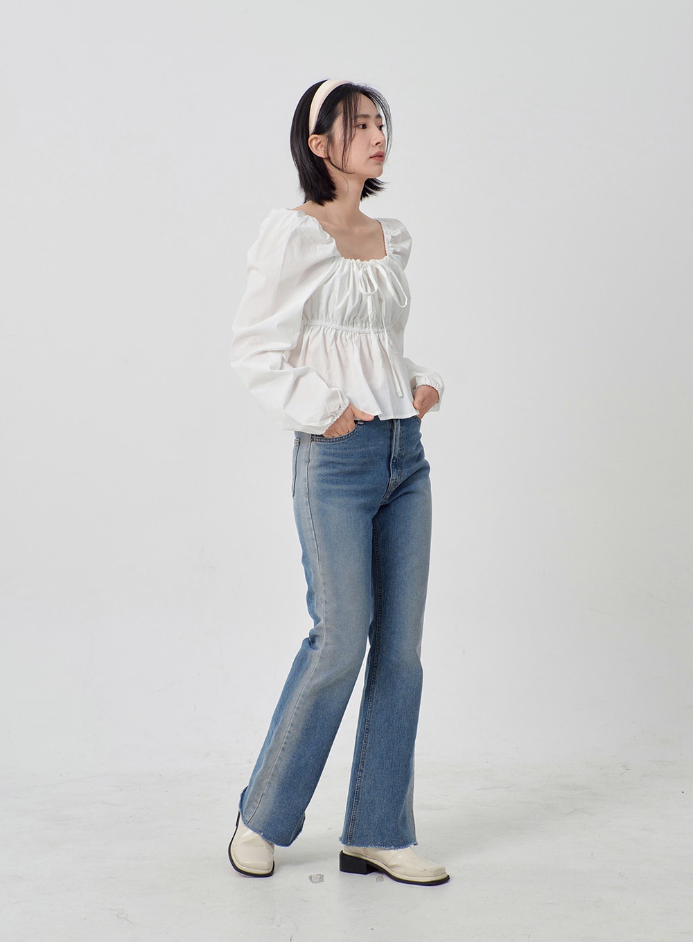 Light Washed Bootcut Jeans OD27 in light blue, three-quarter side view on model looking away, slim-fit washed cotton bootcut denim, raw frayed hem, styled with white ruffle blouse and white block-heel loafers.