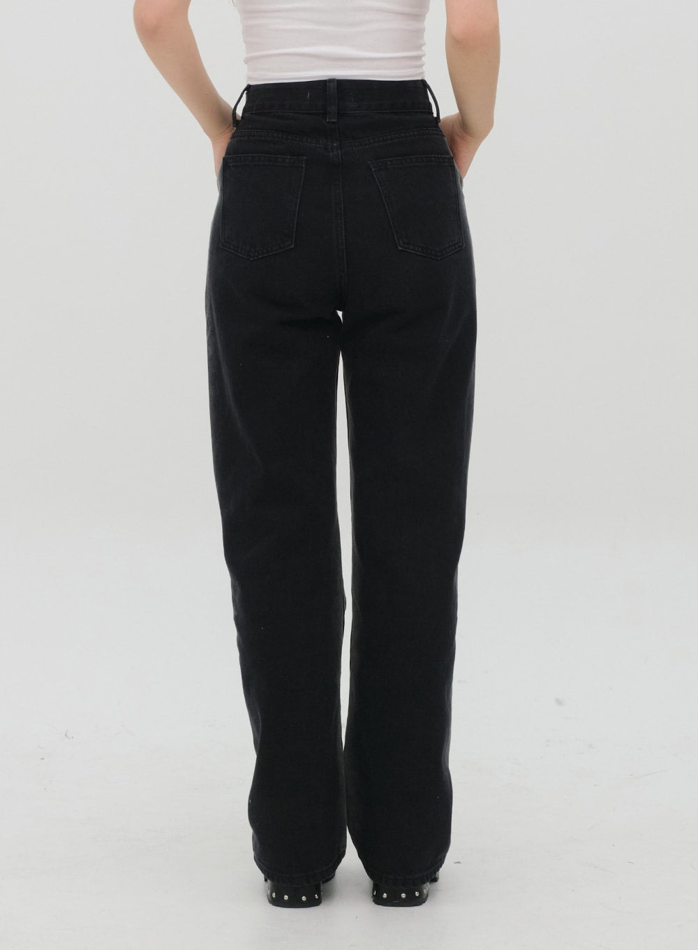 Black Jeans C1002 in washed black, back view on model, two back patch pockets with stitching, high-rise waist, wide straight leg, full-length cotton denim, styled with white top.