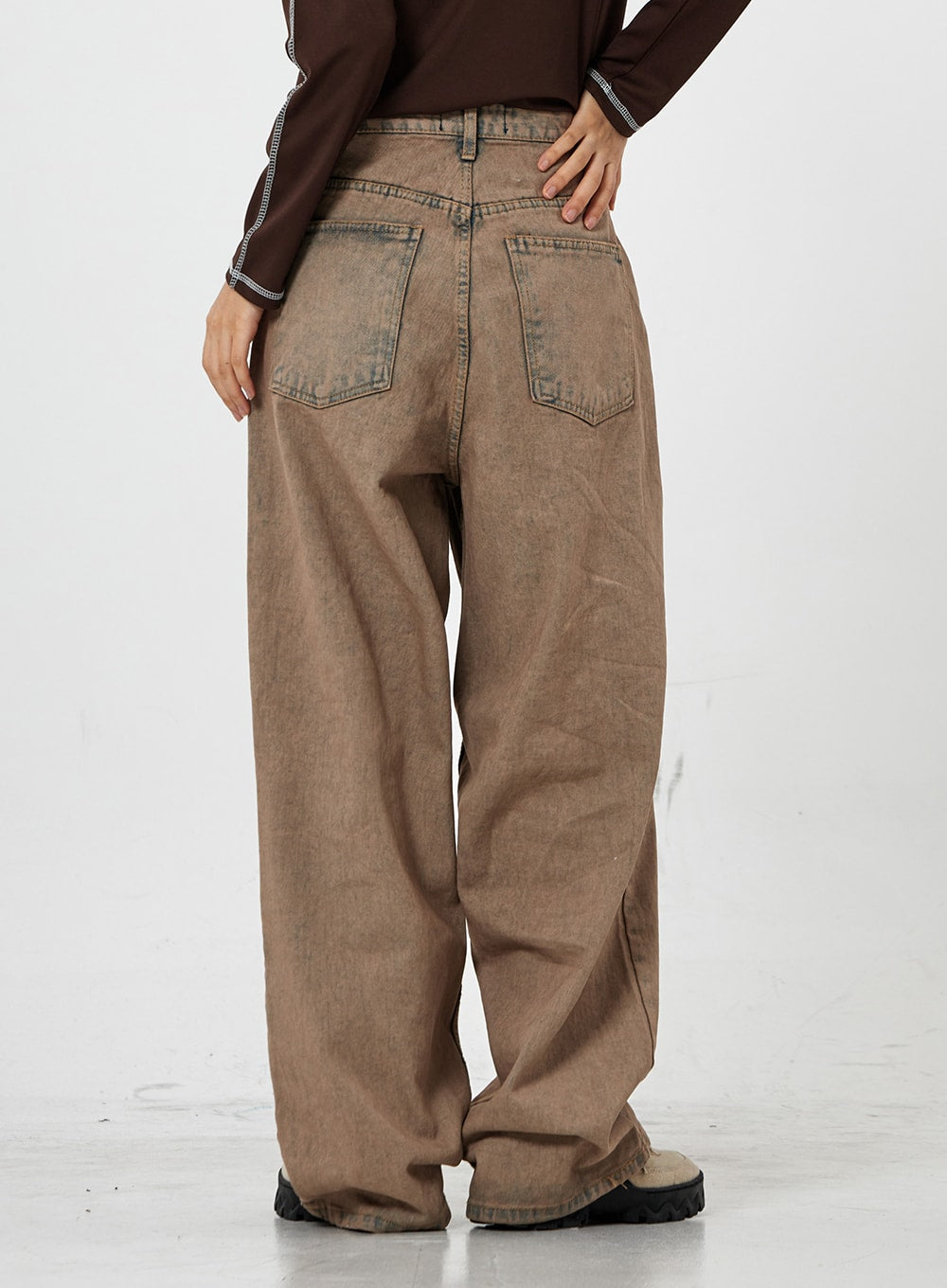 Raemon Wide Jeans Unisex CS21 in brown acid-wash, back view from waist to ankle on model, two patch-style back pockets and wide pooling hem on chunky-soled shoes.