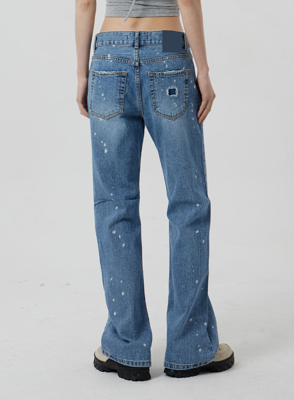 Low Rise Bootcut Jeans CF309 in blue denim, back close-up on model from waist to hem, rear patch pockets with logo label, paint-splatter distressing, subtle bootcut flare visible at hem.
