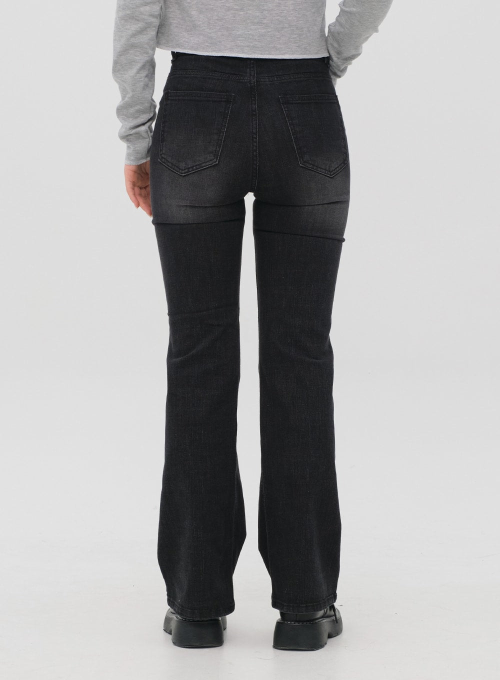 Bootcut Jeans M4 in black gradation wash, back view close-up on model, rear patch pockets with stitching detail, bootcut flare, gradation wash from dark waist to lighter hem.