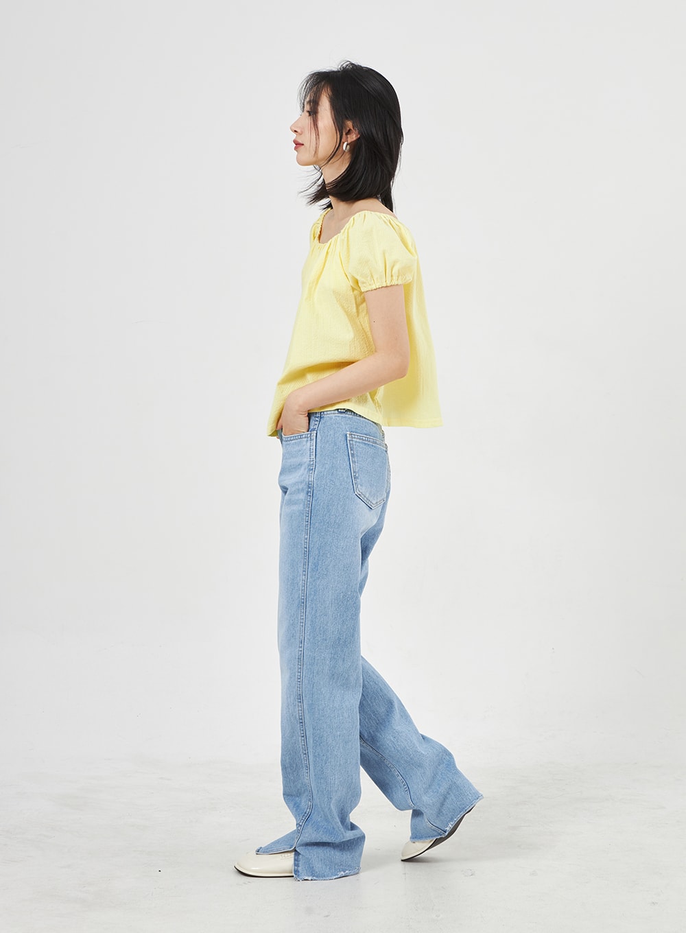 Light Wash Jeans OA310 in light blue, side profile shot on model walking, wide-leg washed denim showing straight silhouette and slit at hem, styled with yellow crop top.
