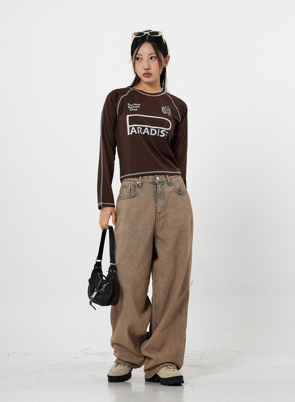 Raemon Wide Jeans Unisex CS21 in brown acid-wash, full-length front view on model facing slightly left, wide-leg cotton denim with vintage fade, paired with crop moto tee and mini bag.