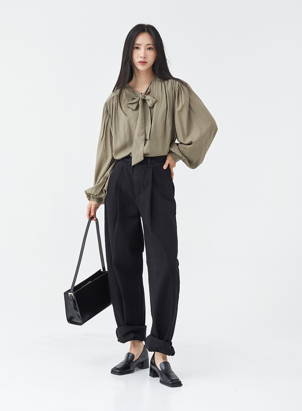 Pintuck Black Jeans OG18 in black, full-body front shot on model holding black tote bag, wide-fit cotton pintuck jeans with rolled hem, styled with olive bow blouse and loafers.