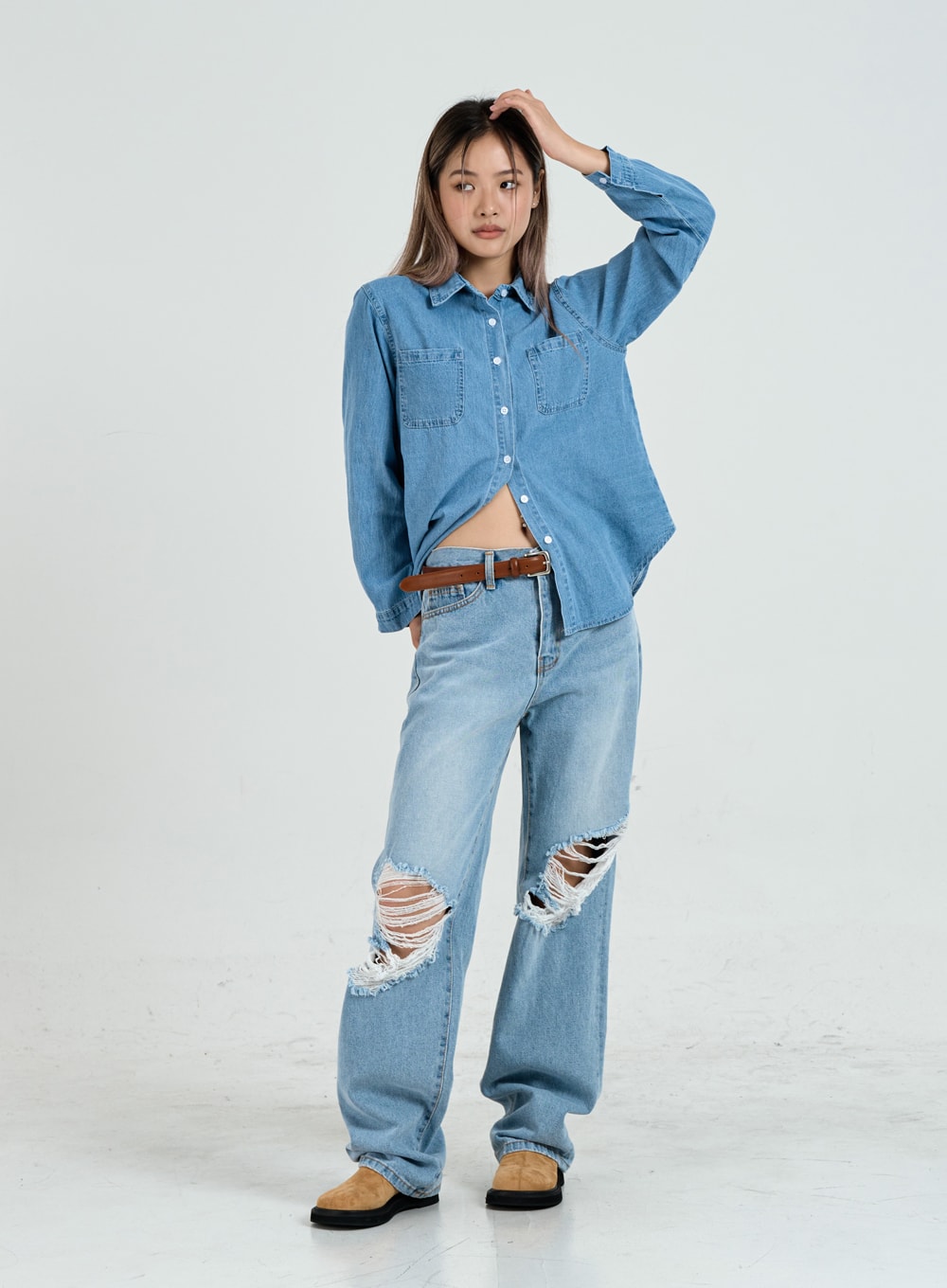 Ripped Maxi Denim Pants Unisex CO14 in light blue, full-body front view on model with hand raised, wide-fit casual denim with large destroyed knee tears, paired with denim shirt and brown belt.