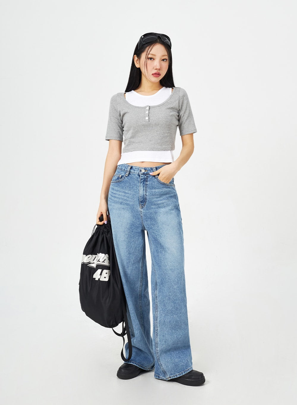 Mid-Wash Bootcut Jeans CM323 in mid blue, full-length front view on model holding drawstring bag, wide-fit high-rise washed denim with bootcut hem, casual street style look.