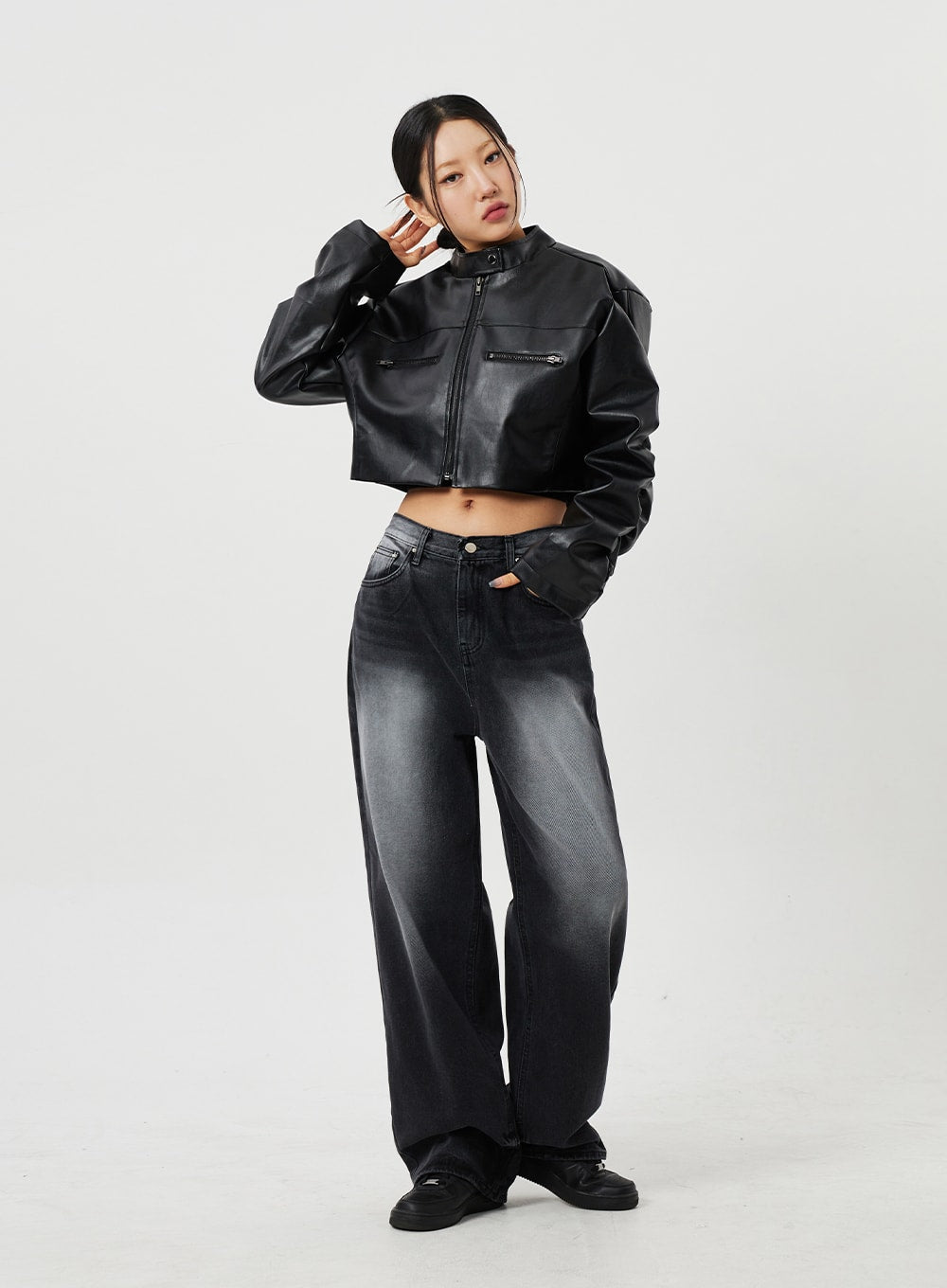 Mid-Rise Baggy Jeans CF328 in black, front three-quarter editorial shot on model, wide-fit washed cotton denim with mid-rise fit, styled with cropped faux-leather jacket, dynamic hand-to-ear pose.