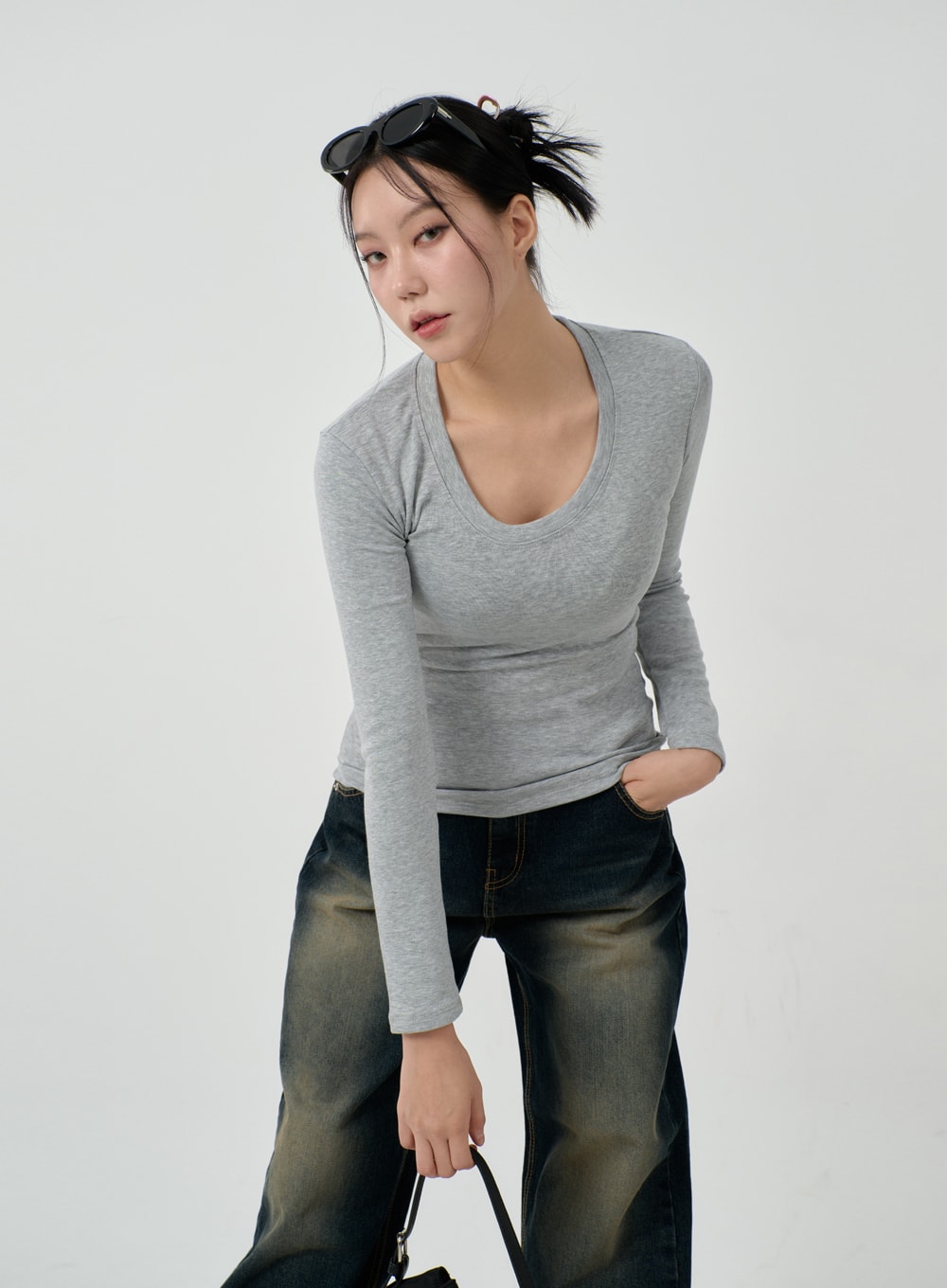 Vintage Washing Baggy Jeans ID23 in dark indigo, upper-body angled close-up on model leaning forward, waistband and faded thigh wash visible, styled with grey top, sunglasses on head, black bag.