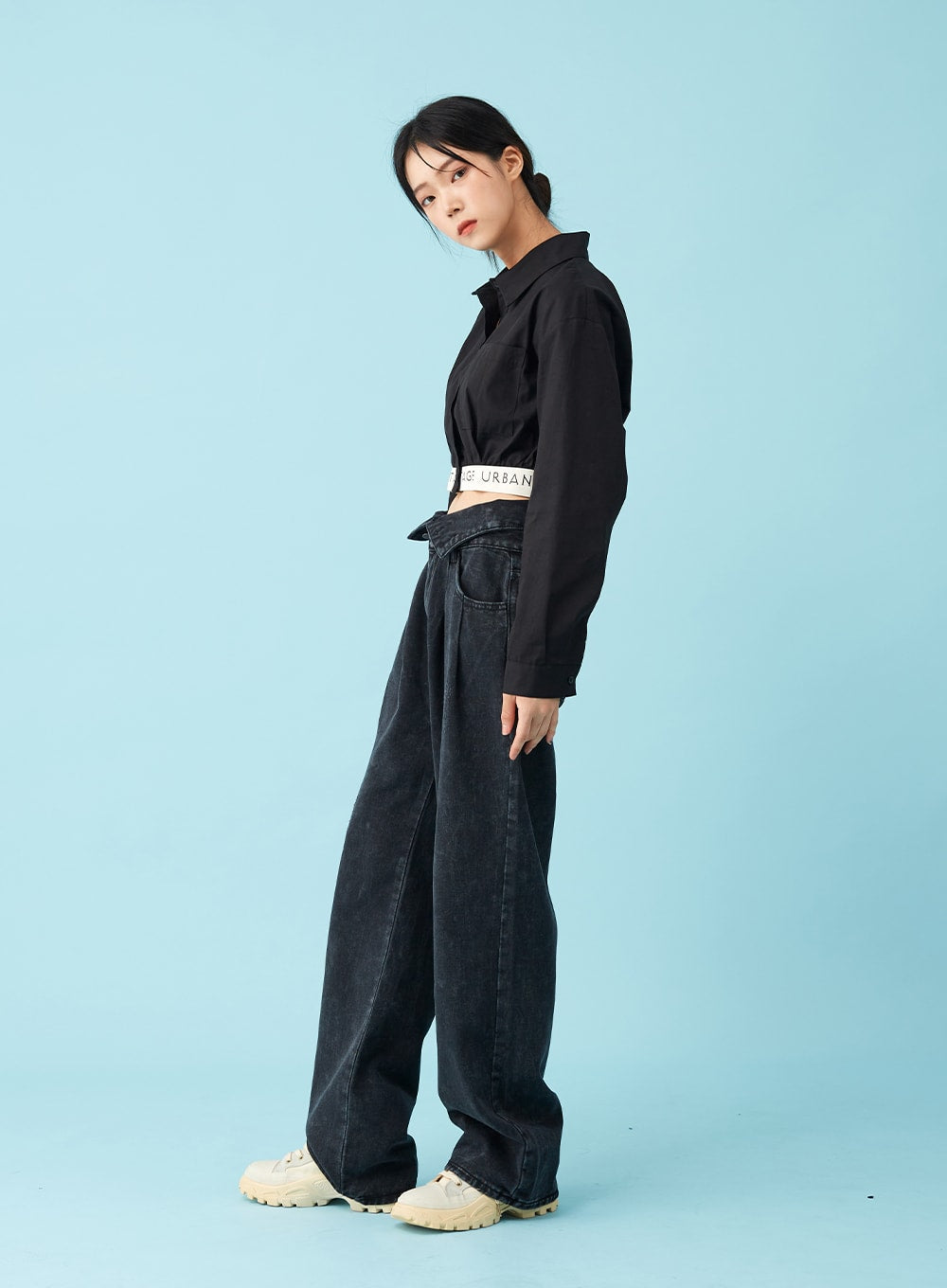 Four Buttoned Open Black Jeans CU8 in washed black, side view on model, wide-leg silhouette and low-rise open waistband profile visible, paired with black crop shirt and logo waistband, chunky sneakers.