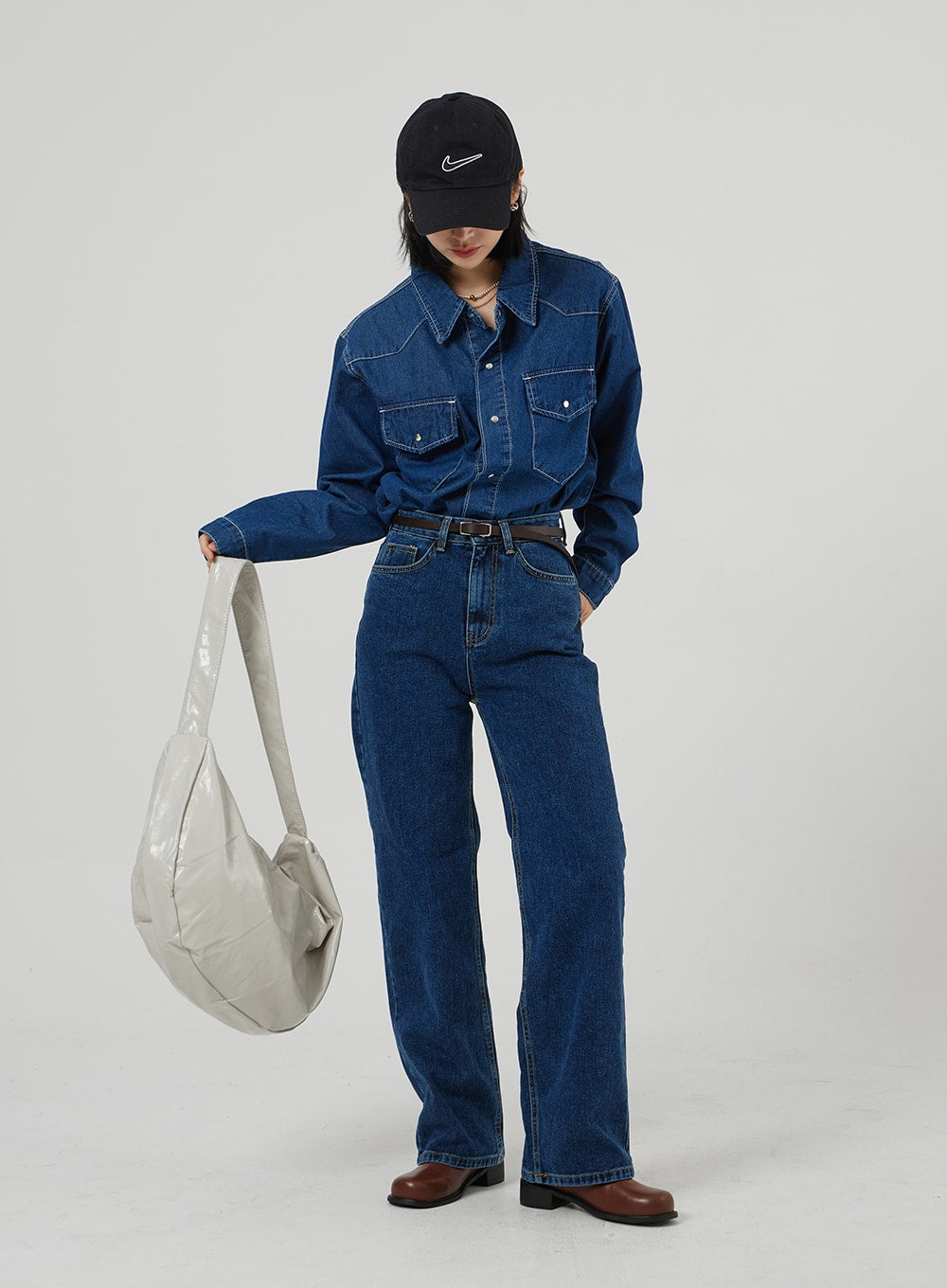 Basic Indigo Jeans OF310 in indigo, full-length front on model looking down holding tote bag, wide-fit straight-leg denim, five-pocket design, belted, styled in head-to-toe denim look.
