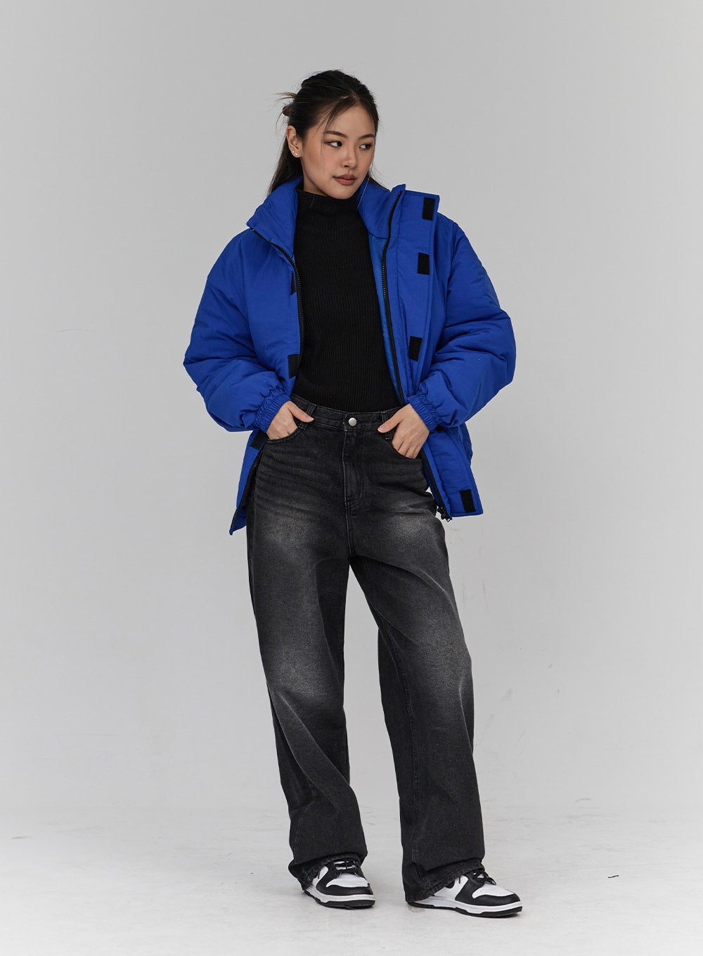 Light Washing Wide Leg Black Jeans CN23 in washed black, three-quarter front view on model, wide-fit washed denim, hands in pockets, paired with blue puffer jacket and black turtleneck.