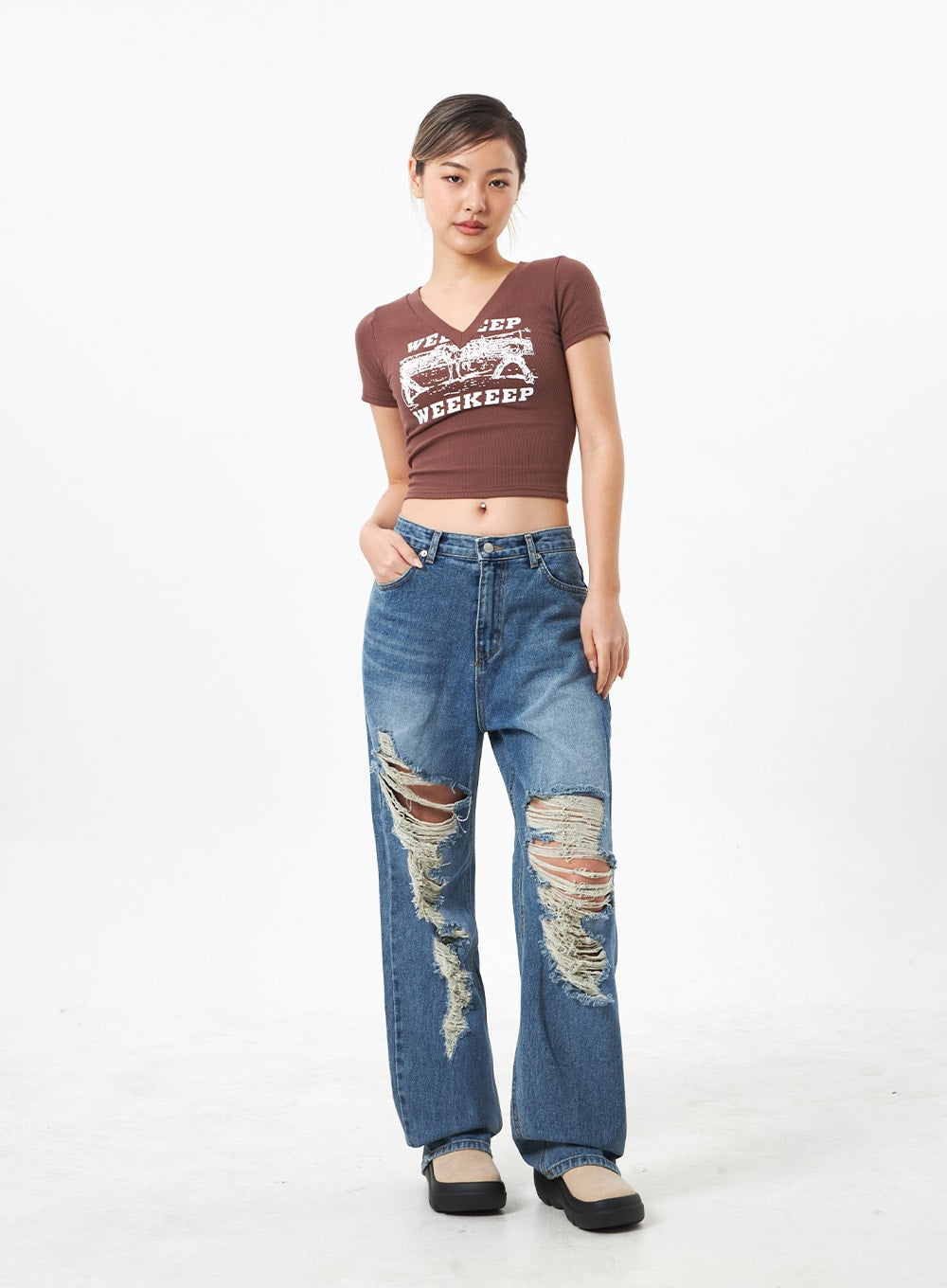 Wide Ripped Jeans CA304 in medium blue, full-body front on model with slight angle, wide-fit distressed denim with multiple knee rips and frayed threads, styled with brown graphic crop tee.