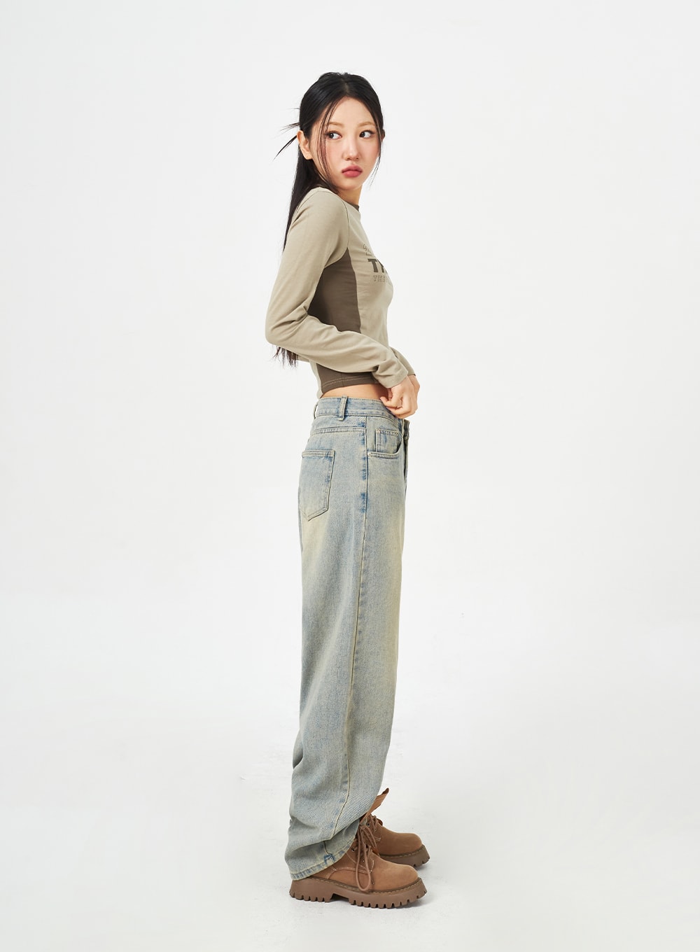Light Blue Baggy Jeans CM323 in light blue, full-length side profile on model looking back, floor-grazing wide leg with yellow-tinted fade, styled with khaki crop top and lug-sole boots.