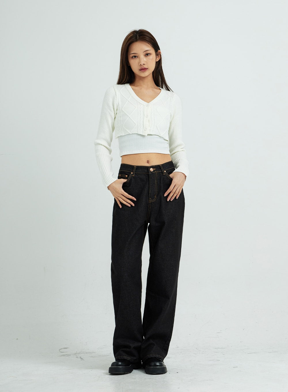 Pepe Wide Pants CS15 in black, full-length front view on model, wide-leg cotton denim with contrast stitching, styled with white ribbed cropped cardigan, hands in pockets.